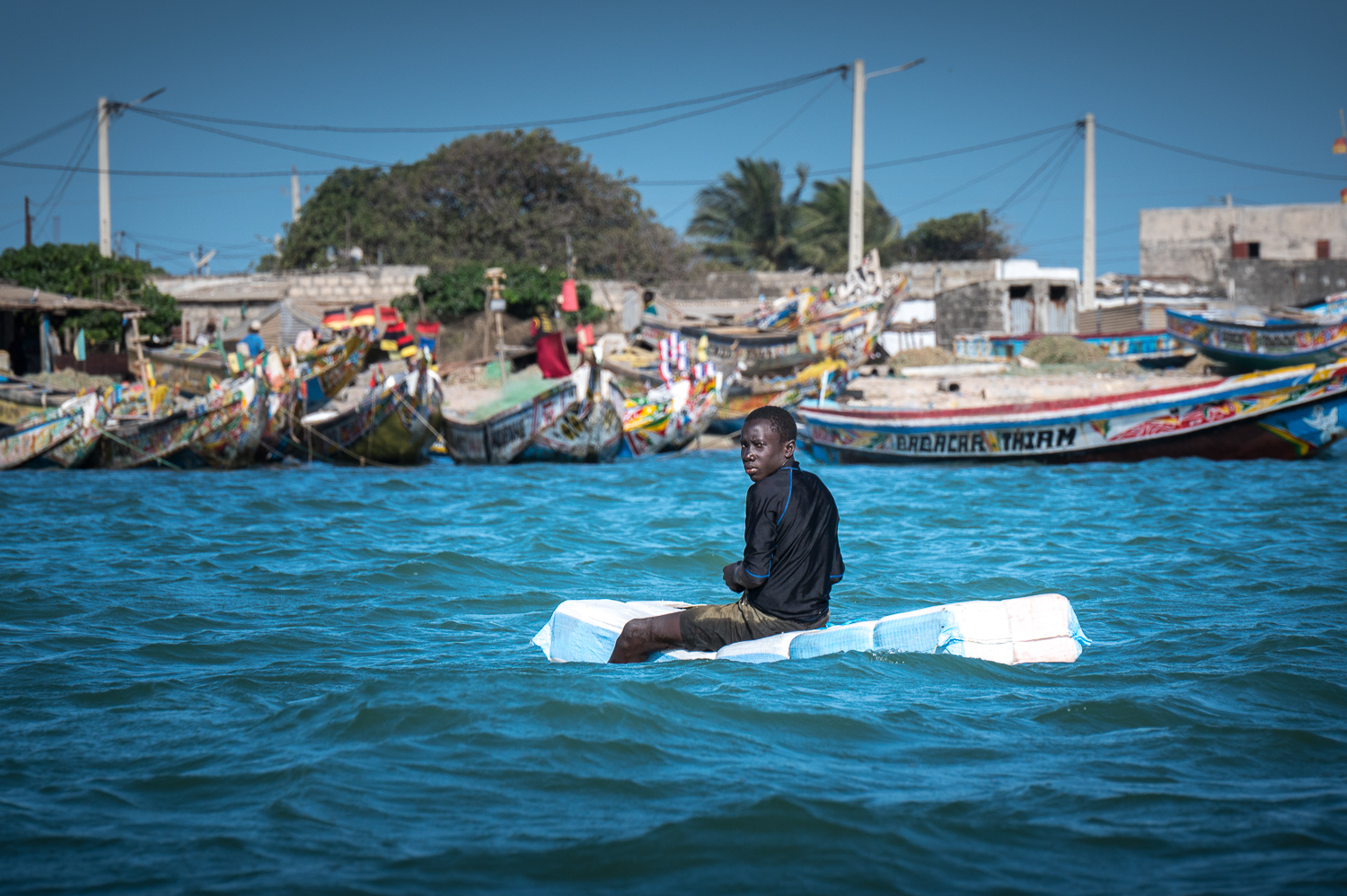 Jeune pêcheur sur des bidons dans le port de Djiffer